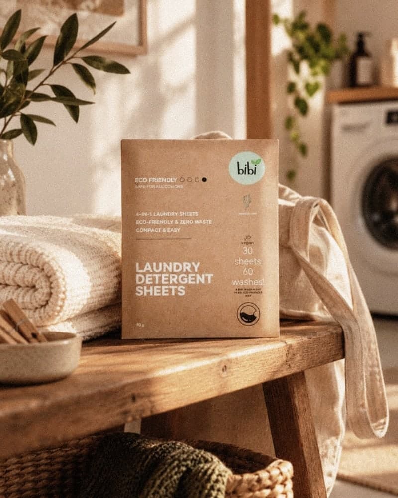 Een pakje bibi wasstrips op een houten bankje in de bijkeuken, met opgevouwen handdoeken en een wasmachine op de achtergrond